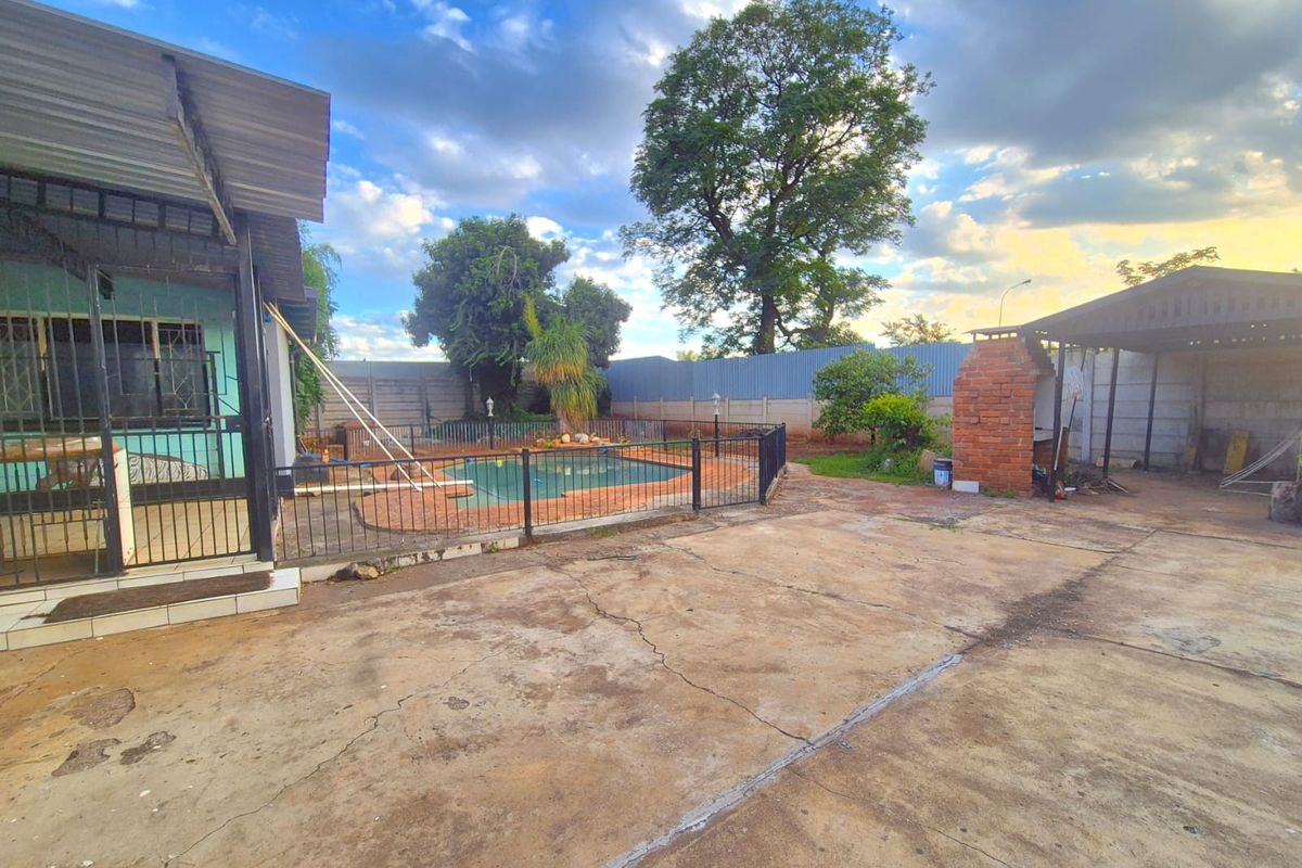 Rear garden area featuring a swimming pool, brick braai, and extensive concrete paving, providing a functional outdoor entertainment space.