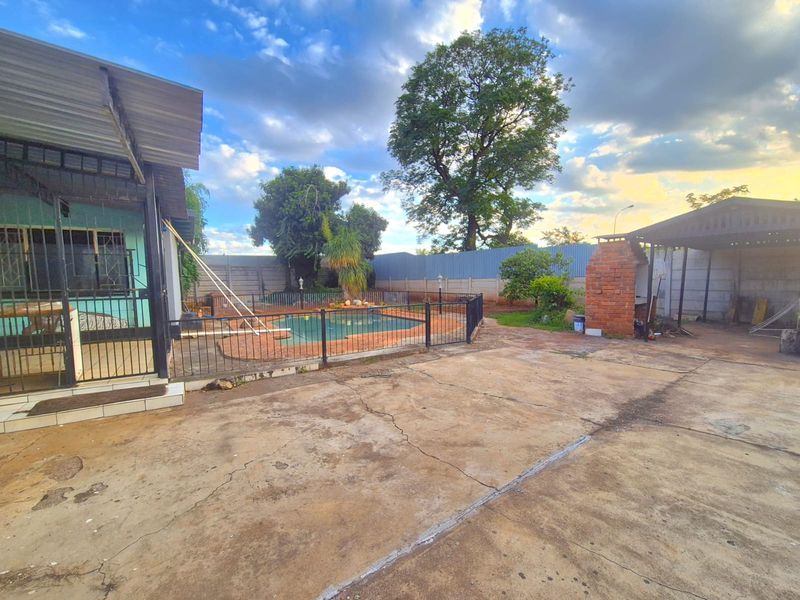 Rear garden area featuring a swimming pool, brick braai, and extensive concrete paving, providing a functional outdoor entertainment space.