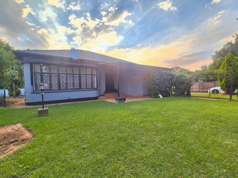 Front view of a house featuring a covered porch, leaded glass windows, and a well-maintained lawn under a sunset sky.