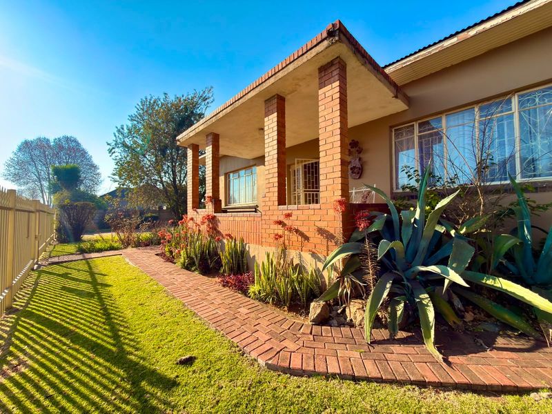 Front elevation of a house featuring a covered porch with brick pillars, a brick walkway, and established garden landscaping.