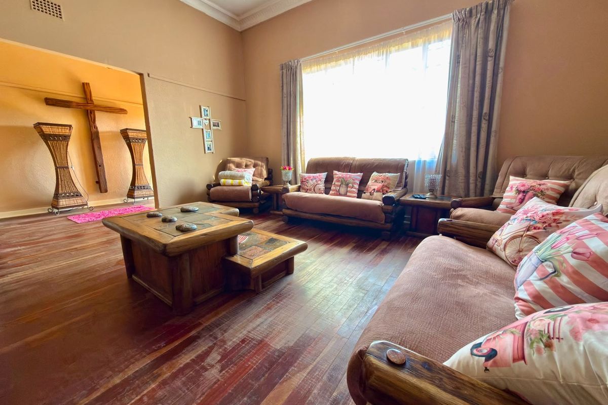 A spacious living room featuring original hardwood flooring, ornate ceiling cornicing, and a large window allowing for ample natural light.