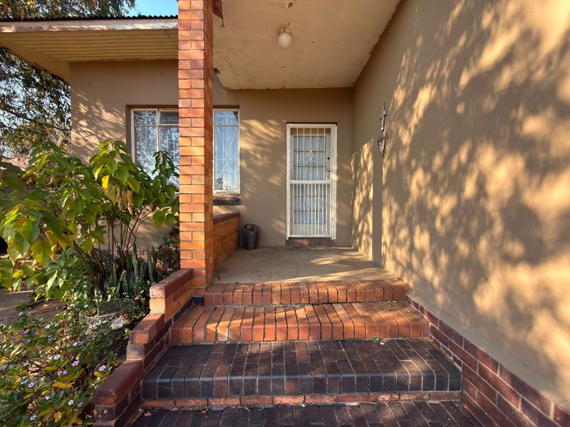 Front entrance area featuring brick steps, a covered porch, and a security gate, showing signs of wear and weathering.