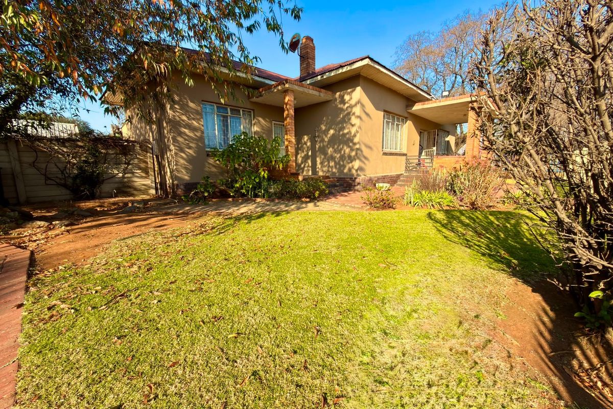 Rear view of the house featuring a covered patio, brick chimney, and a spacious garden area with established landscaping.