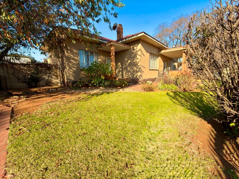 Rear view of the house featuring a covered patio, brick chimney, and a spacious garden area with established landscaping.