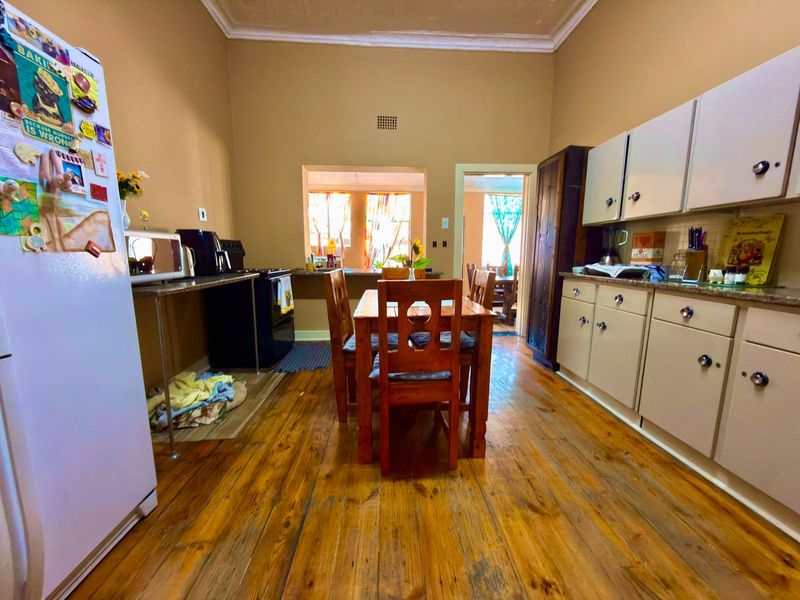 A functional kitchen featuring timber flooring, fitted cabinetry, and a central dining area with access to an adjoining room.