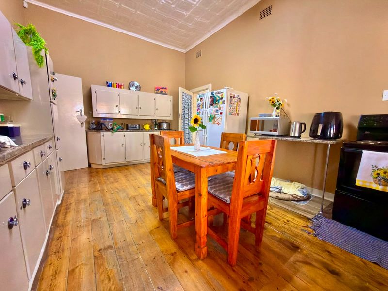 A spacious kitchen featuring timber flooring, pressed metal ceilings, and ample built-in cabinetry with stone countertops, offering a functional and character-filled cooking and dining space.