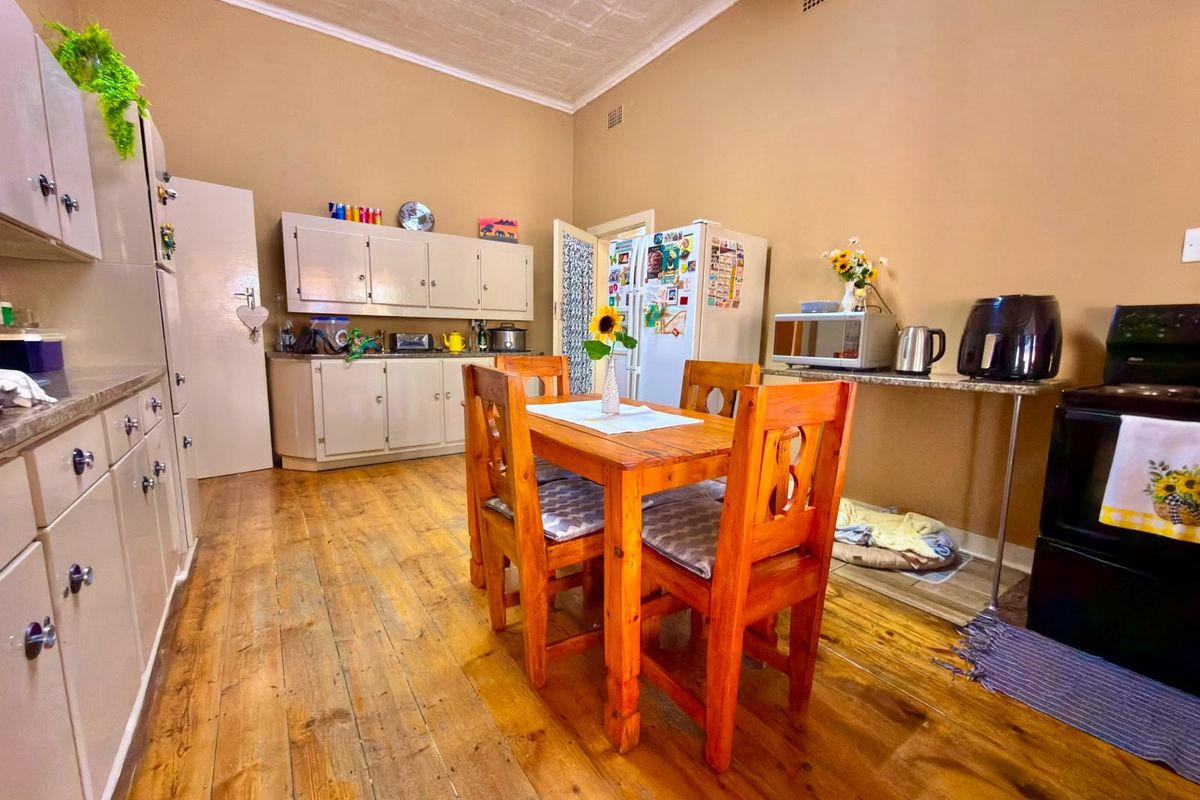 A spacious kitchen featuring timber flooring, pressed metal ceilings, and ample built-in cabinetry with stone countertops, offering a functional and character-filled cooking and dining space.