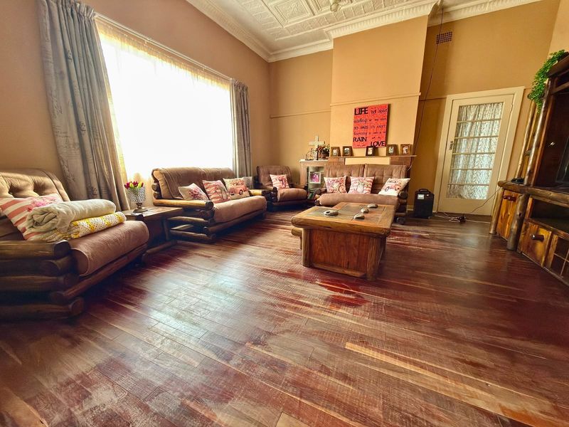 Spacious living room featuring original timber flooring, an ornate pressed metal ceiling, and a traditional fireplace mantle.