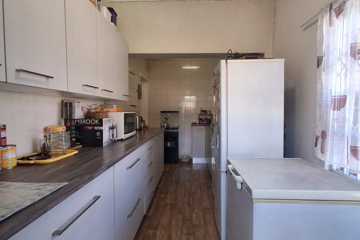 A functional galley-style kitchen featuring white cabinetry, dark laminate countertops, and wood-look vinyl flooring, requiring some cosmetic updates to the ceiling and finishes.