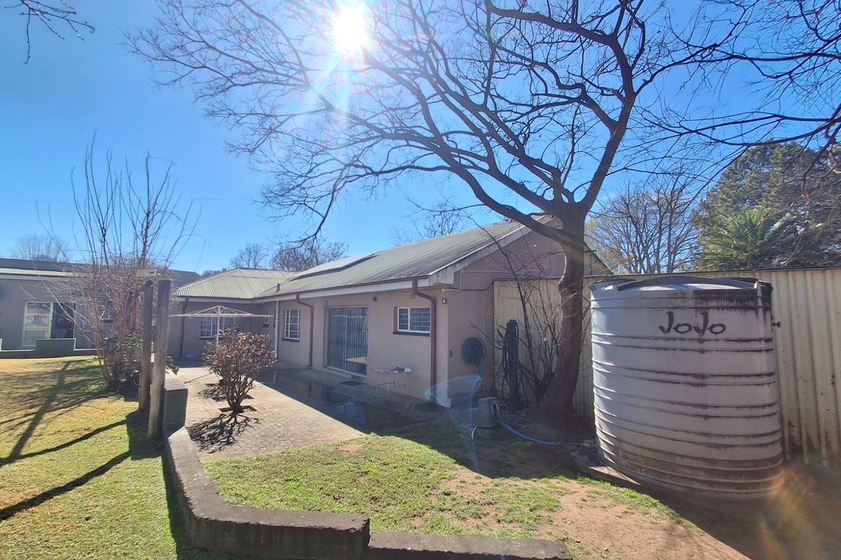 Rear view of the property featuring a paved patio area, retaining wall, and a large water storage tank set within the garden.