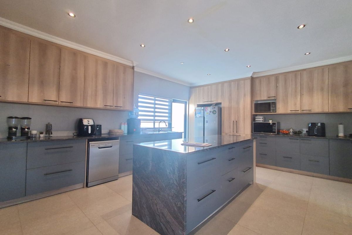 Modern kitchen featuring a large central island with stone countertops, extensive two-tone cabinetry, and high-quality integrated appliances.