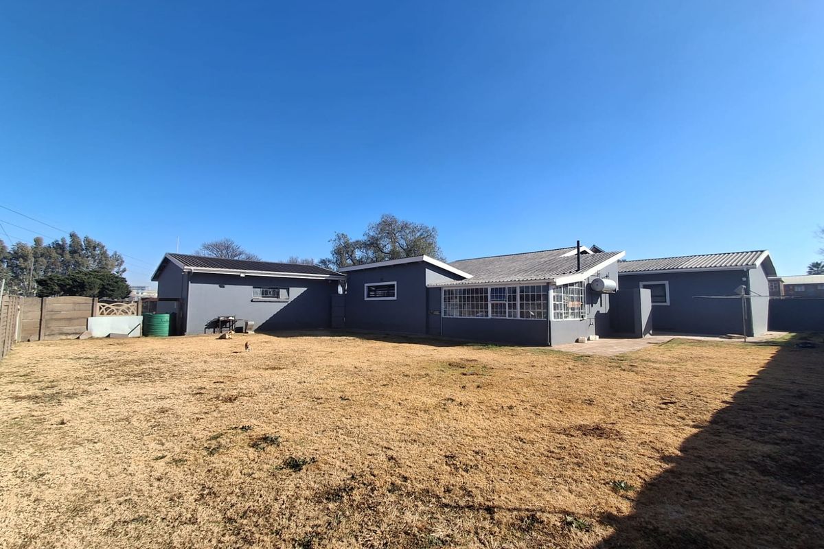 Rear view of the property featuring a large garden, paved patio area, and enclosed sunroom with corrugated metal roofing.