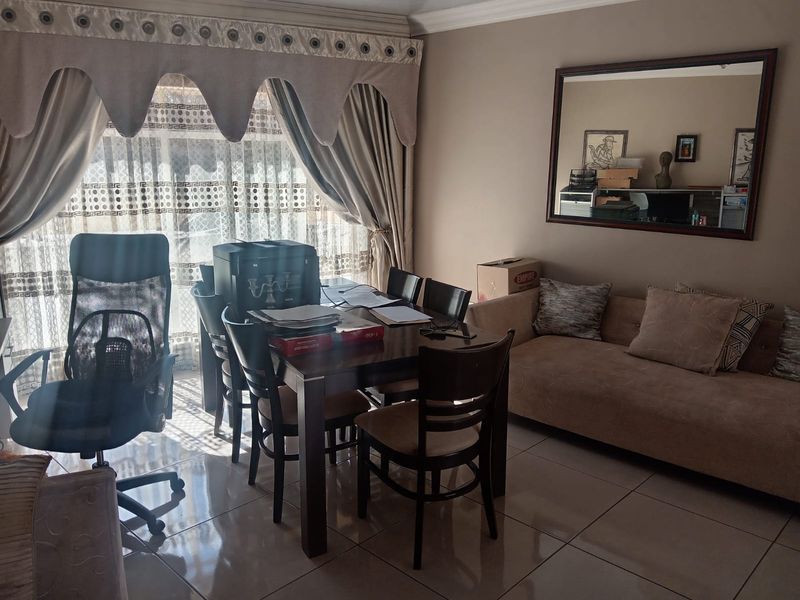 A living room area featuring tiled flooring, decorative cornicing, and a curtain pelmet, providing a functional space for relaxation and dining.
