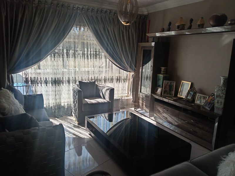 A well-maintained living room featuring tiled flooring, built-in cabinetry, and large windows with elegant drapery, creating a comfortable and inviting atmosphere.