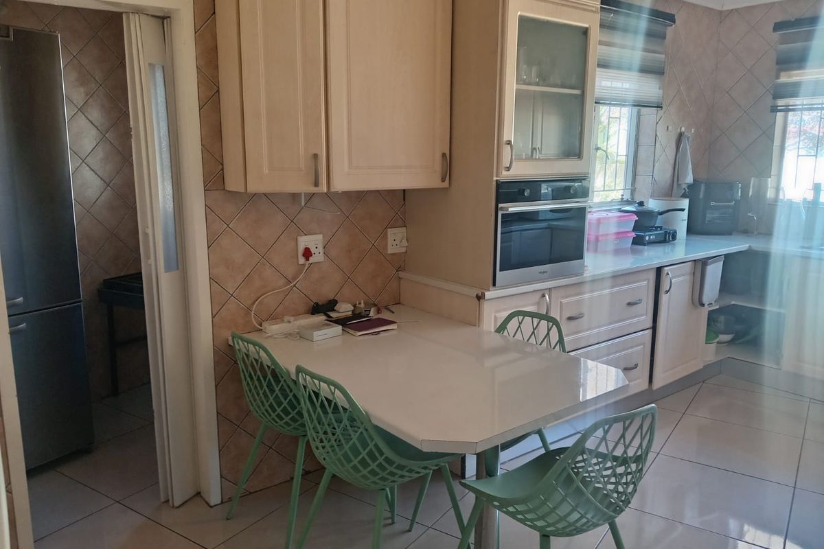 A functional kitchen featuring built-in cabinetry, a wall-mounted oven, tiled backsplash, and tiled flooring, with an adjacent doorway leading to a utility area.