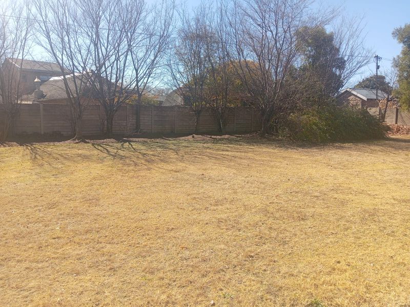 A spacious, open garden area featuring a precast concrete boundary wall and mature trees, offering potential for landscaping and outdoor development.