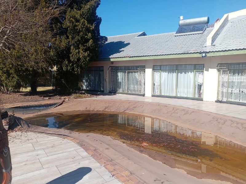 Rear exterior view featuring a swimming pool with a damaged cover, tiled patio area, and solar water heating system on the roof.