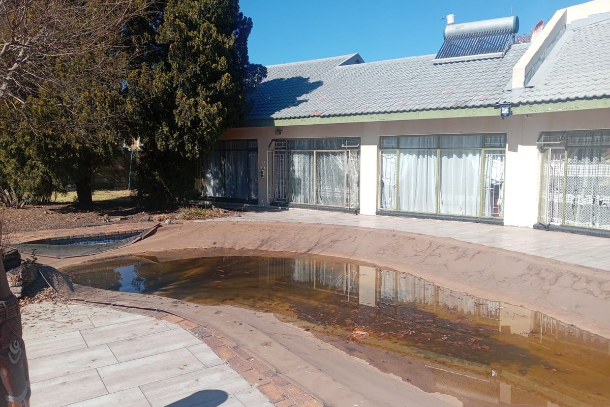 Rear exterior view featuring a swimming pool with a damaged cover, tiled patio area, and solar water heating system on the roof.