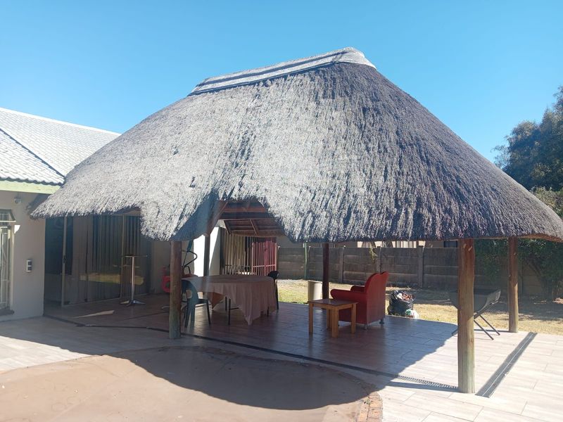 A covered outdoor patio area featuring a traditional thatched roof, tiled flooring, and timber support posts, providing a shaded space for outdoor living.