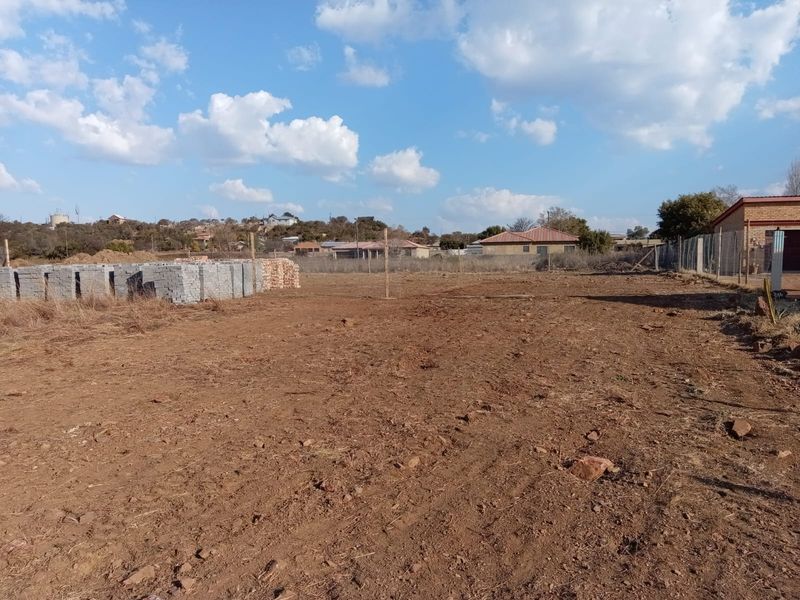 A vacant residential plot featuring cleared earth, wire mesh perimeter fencing, and a stack of concrete building blocks ready for construction.
