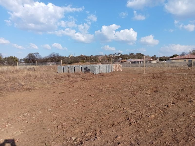 A vacant residential plot featuring cleared earth, wire perimeter fencing, and a stack of construction materials ready for development.