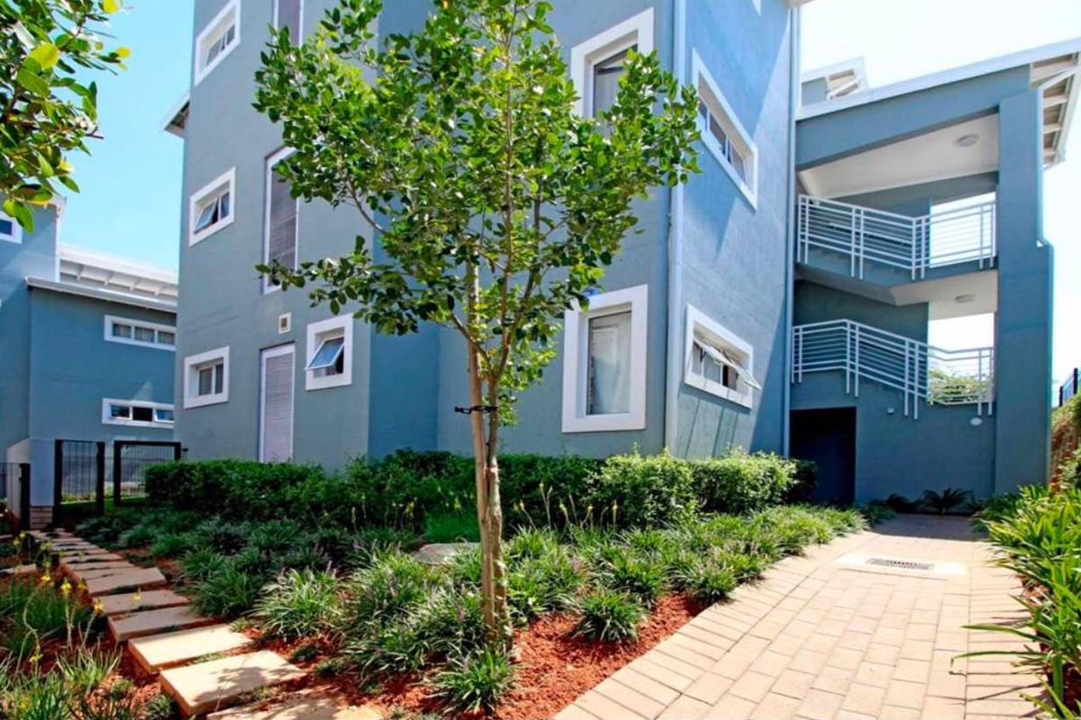 A well-maintained exterior view of the apartment building featuring a landscaped garden, paved walkways, and external stair access.