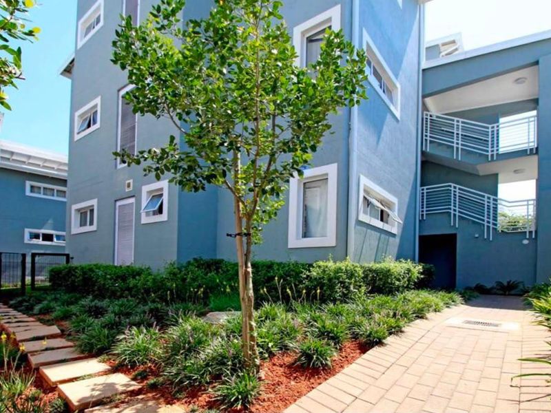 A well-maintained exterior view of the apartment building featuring a landscaped garden, paved walkways, and external stair access.