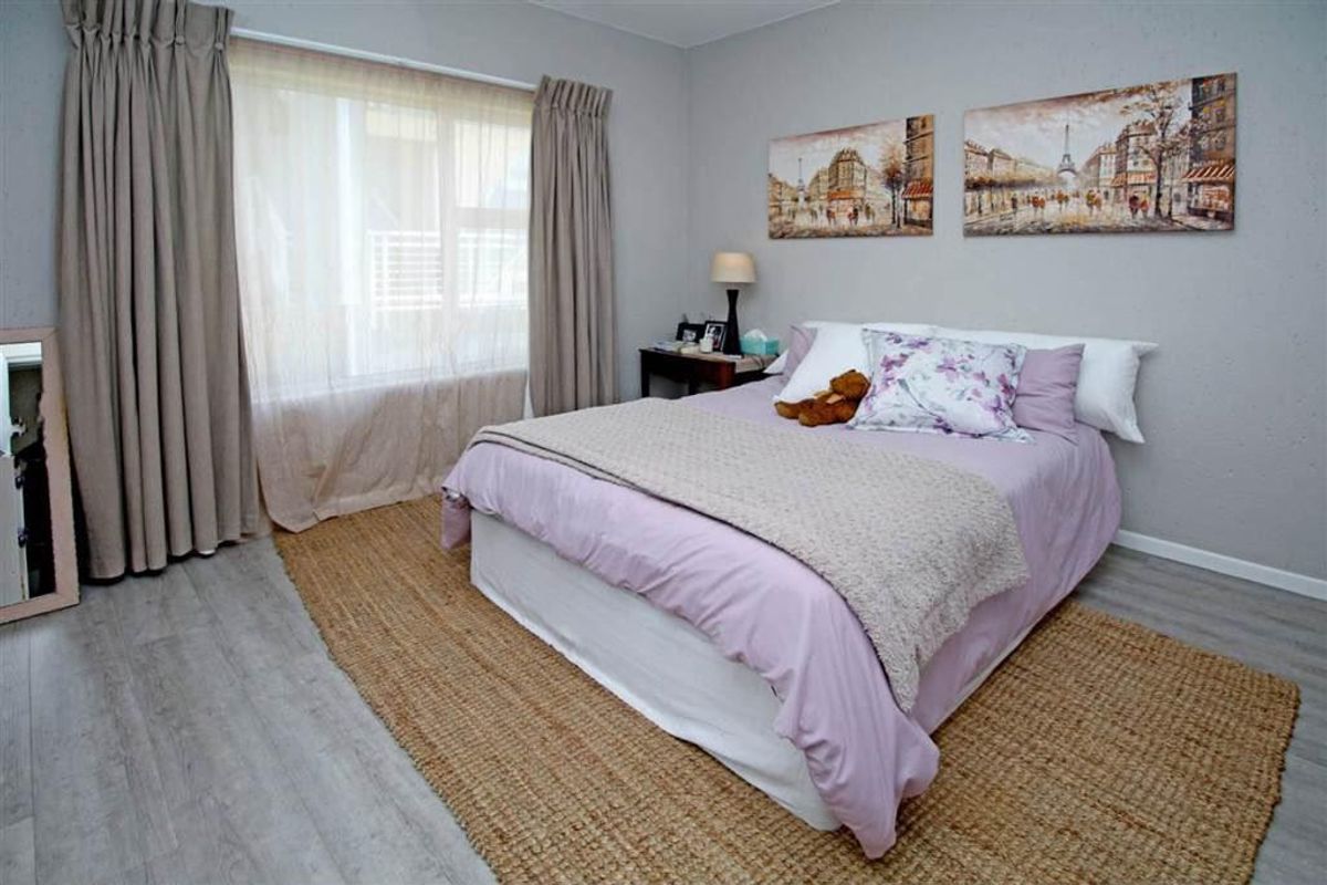 A well-maintained bedroom featuring light-toned laminate flooring, neutral wall finishes, and large windows with installed curtain tracks.