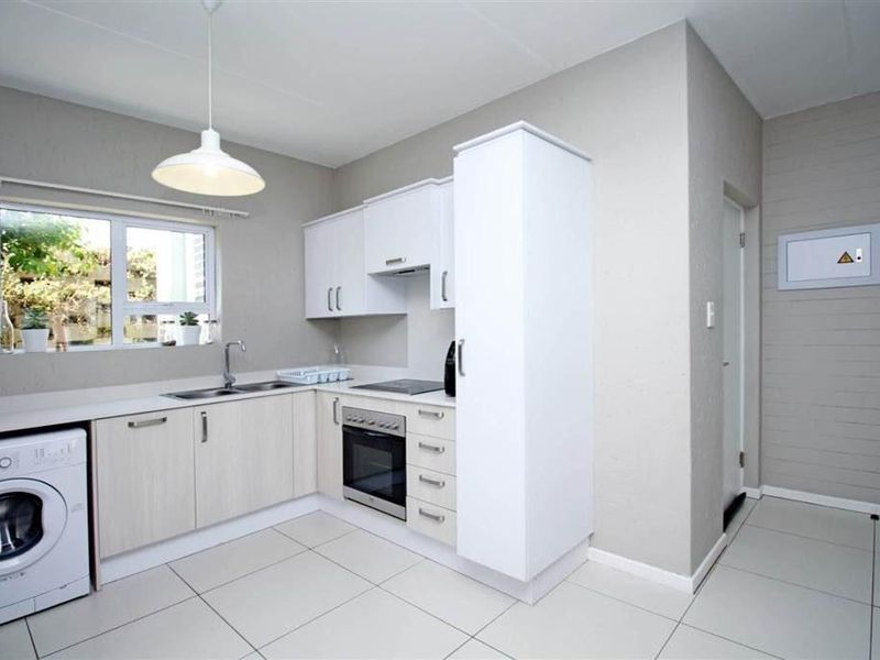 Modern kitchen featuring light-toned cabinetry, built-in oven and hob, integrated laundry space, and tiled flooring with ample natural light.