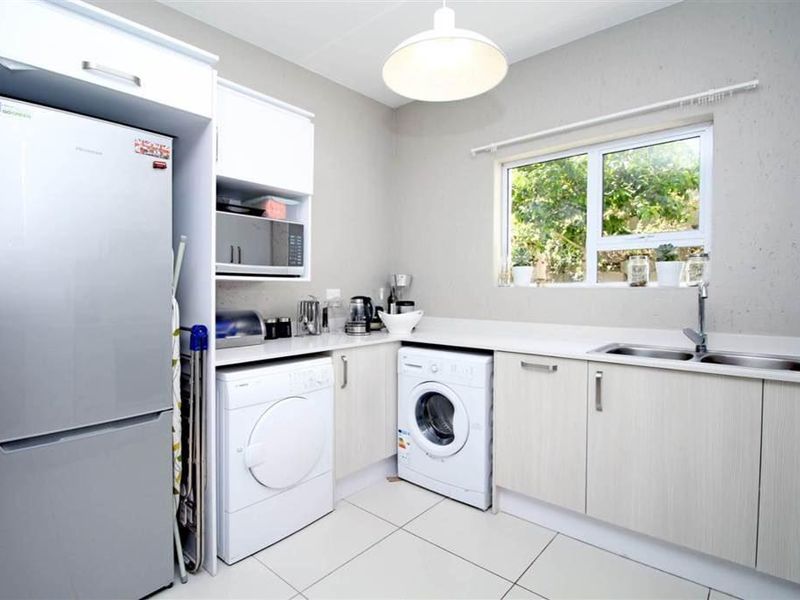 A clean and functional kitchen featuring light-toned cabinetry, tiled flooring, a double basin sink, and dedicated space for laundry appliances.