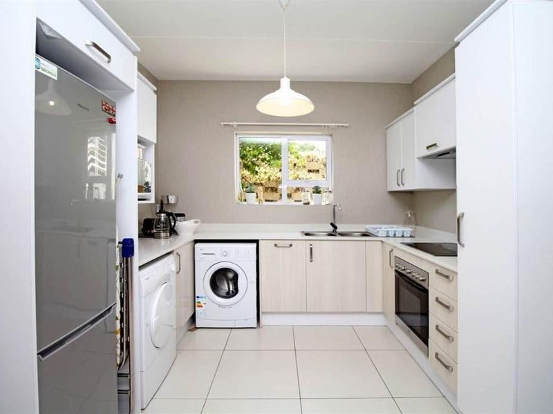 A clean, functional kitchen featuring modern white cabinetry, integrated appliances, tiled flooring, and a window providing natural light.