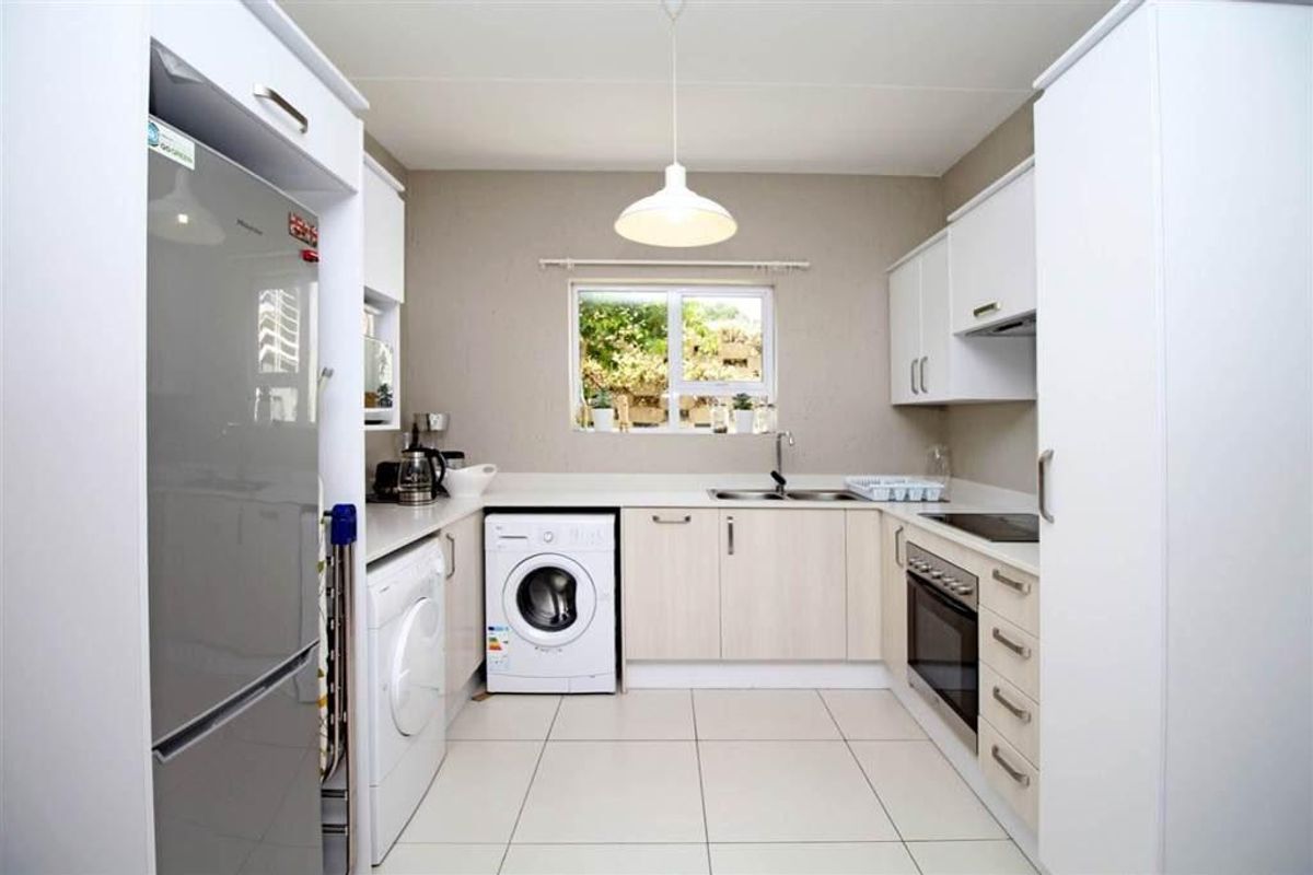 A clean, functional kitchen featuring modern white cabinetry, integrated appliances, tiled flooring, and a window providing natural light.