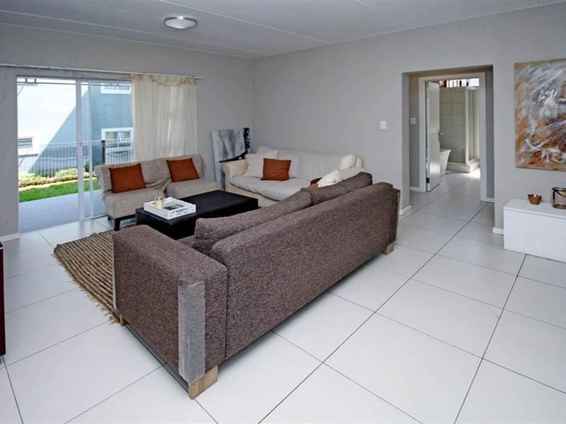 Spacious living room featuring neutral ceramic floor tiles, a sliding glass door leading to the patio, and direct access to an adjacent bathroom.