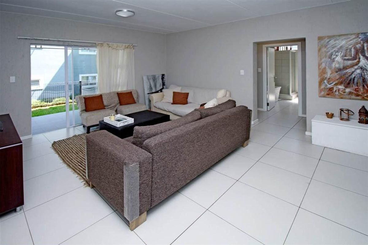Spacious living room featuring neutral ceramic floor tiles, a sliding glass door leading to the patio, and direct access to an adjacent bathroom.