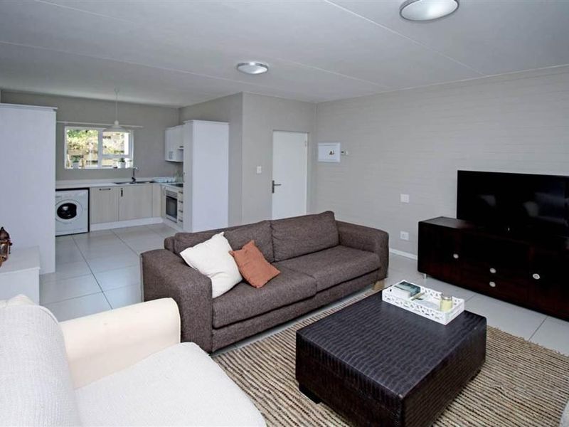 Open-plan living area featuring tiled floors, a functional kitchen with built-in cabinetry, integrated appliances, and laundry plumbing, creating a versatile and connected living space.