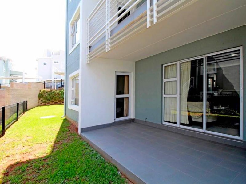 A covered tiled patio area with sliding glass door access, overlooking a private lawn and garden space.