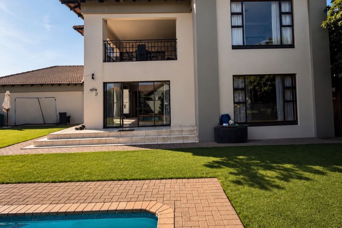Rear view of a two-story house featuring a swimming pool, paved patio area, and an upper-level balcony with sliding glass doors.