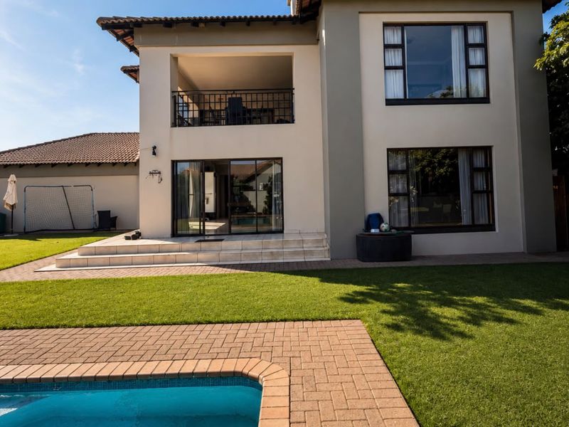 Rear view of a two-story house featuring a swimming pool, paved patio area, and an upper-level balcony with sliding glass doors.