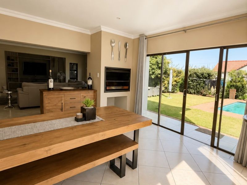 Spacious open-plan living and dining area featuring a built-in fireplace, large sliding glass doors, and direct access to the garden and pool area.