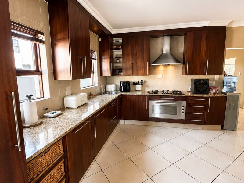 A well-maintained kitchen featuring dark wood cabinetry, granite countertops, stainless steel appliances, and neutral tiled flooring.