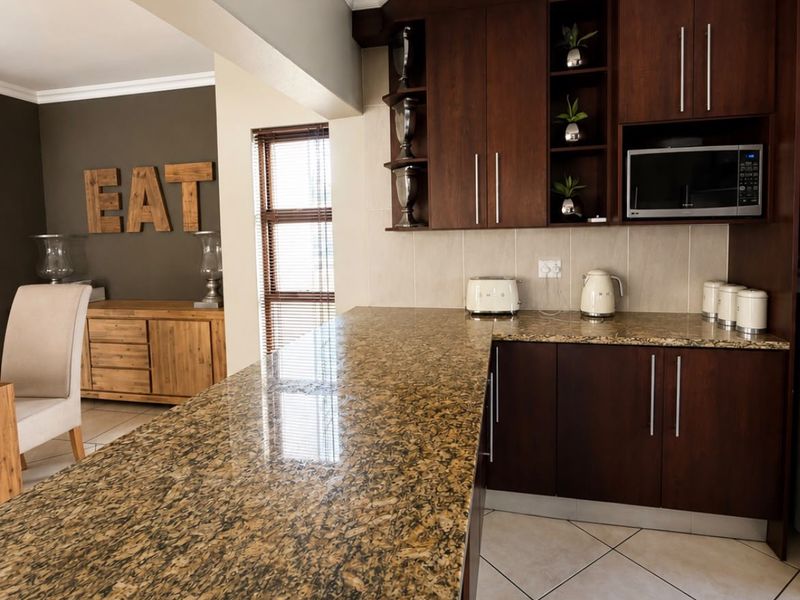A functional kitchen featuring dark wood cabinetry, granite countertops, and tiled flooring, seamlessly flowing into the adjacent living area.