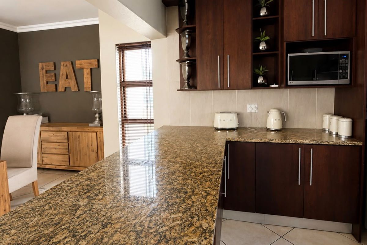 A functional kitchen featuring dark wood cabinetry, granite countertops, and tiled flooring, seamlessly flowing into the adjacent living area.