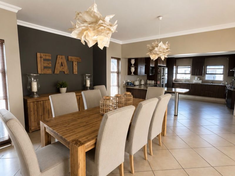 Spacious open-plan dining area flowing into a modern kitchen with dark cabinetry, tiled floors, and elegant pendant lighting.