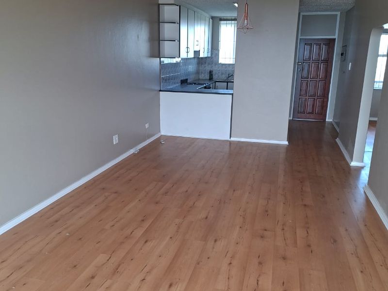 An open-plan living area featuring laminate flooring, a textured ceiling, and an adjoining kitchen space with built-in cabinetry and a breakfast counter.