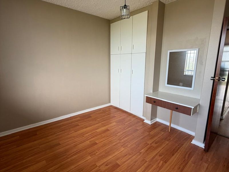 A bedroom featuring laminate flooring, built-in cupboards, and a wall-mounted vanity unit with a mirror.