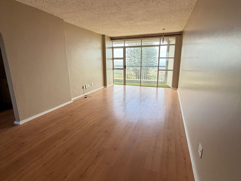 An empty, sunlit living room featuring laminate flooring, a textured popcorn ceiling, and large sliding glass doors leading to an outdoor balcony.