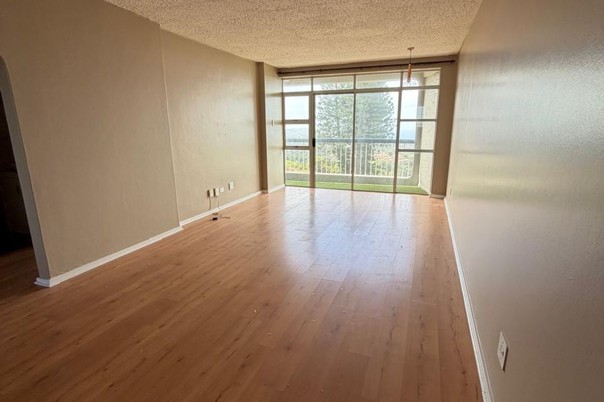 An empty, sunlit living room featuring laminate flooring, a textured popcorn ceiling, and large sliding glass doors leading to an outdoor balcony.