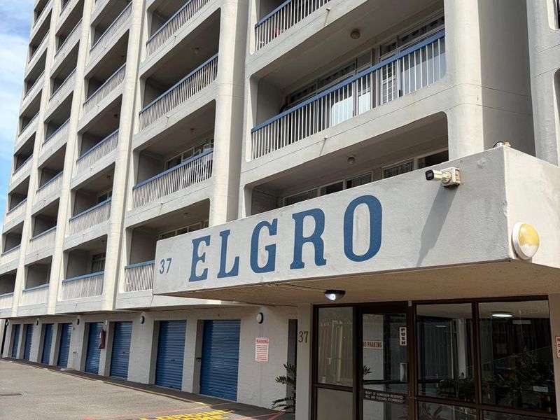 Front elevation of the Elgro apartment building featuring a paved driveway, secure glass entrance, and multiple levels of balconies.