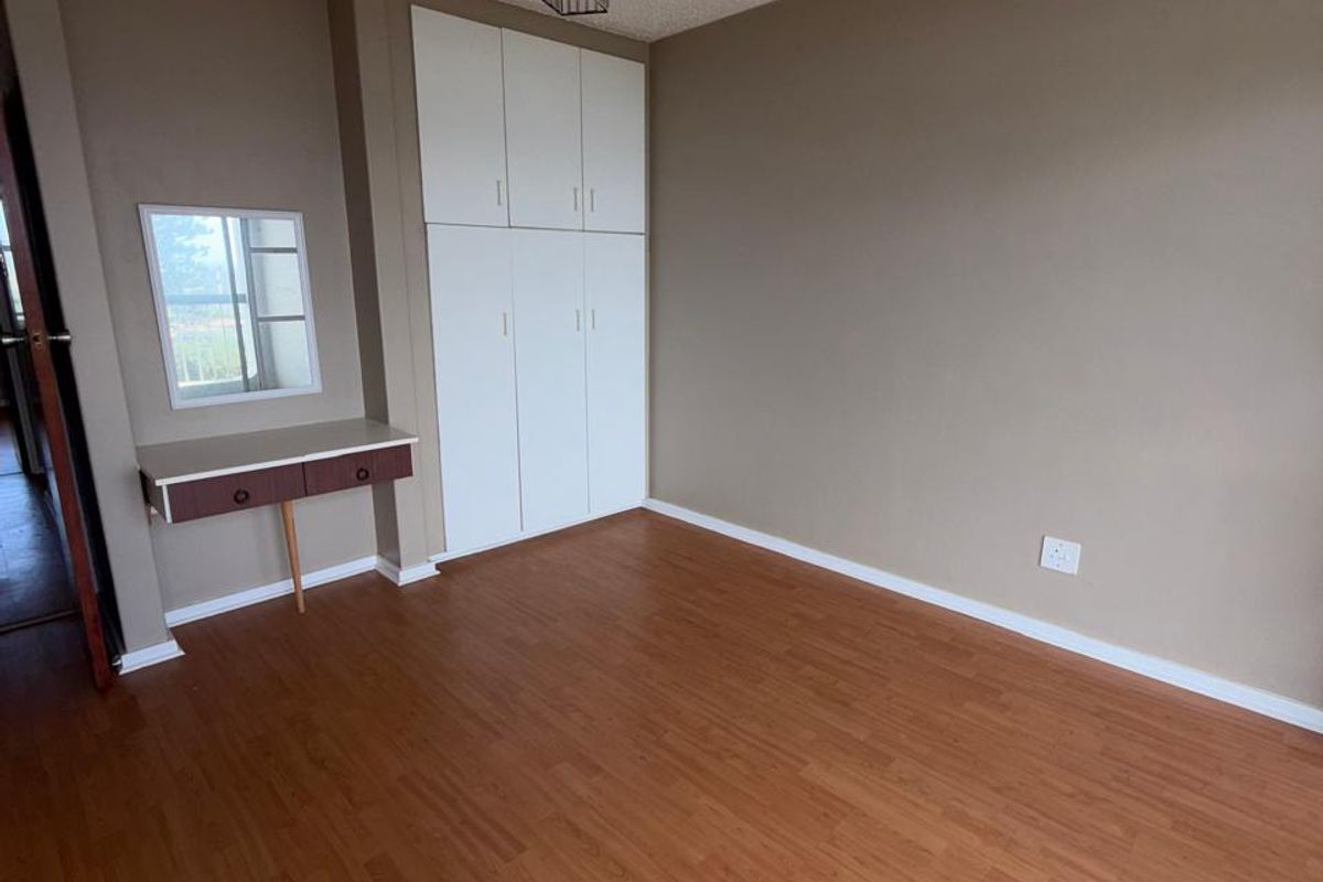 A vacant bedroom featuring laminate flooring, built-in cupboards, and a built-in vanity unit with a mirror.