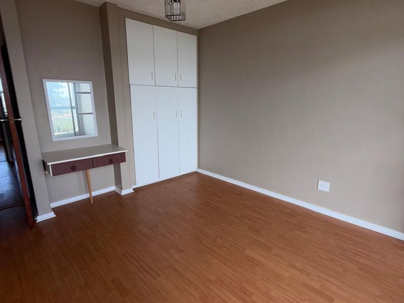 A vacant bedroom featuring laminate flooring, built-in cupboards, and a built-in vanity unit with a mirror.